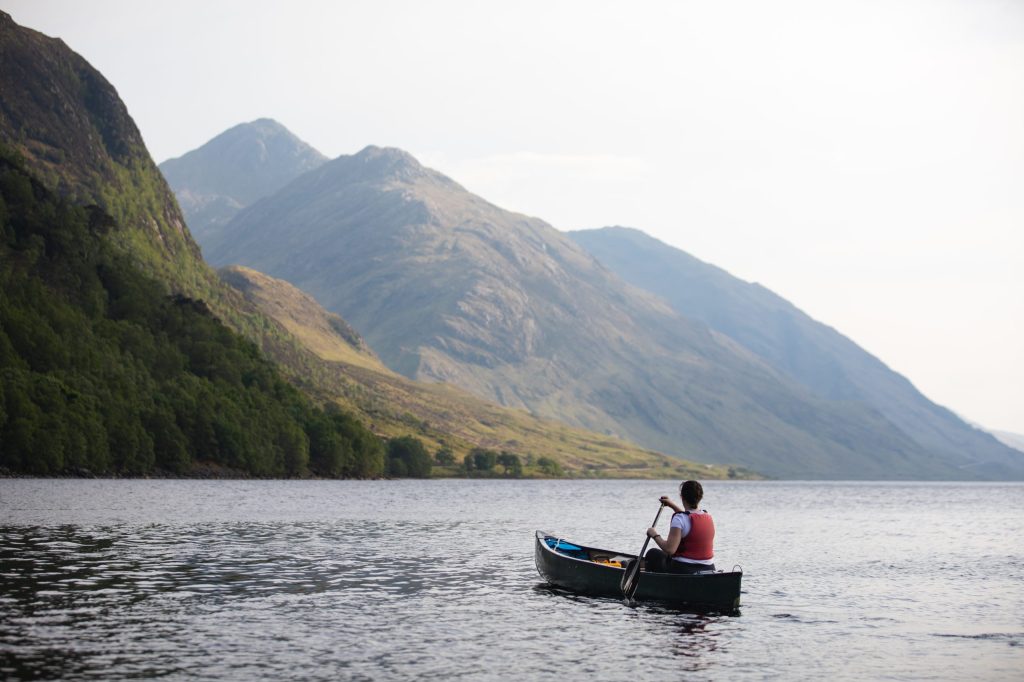 Person paddling a canoe on a lake with mountains in the background.